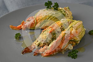 Stuffed zucchini or courgette flowers baked with parmesan cheese and parsley garnish on a gray plate