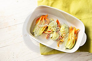 Stuffed zucchini or courgette flowers in a casserole dish on a w