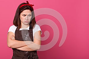 Stuio shot of sad European housewife posing isolated over pink background in studio, looking away, having frowned face, stands
