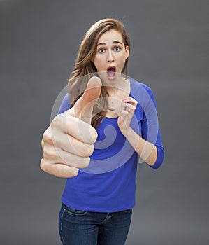 Stunned beautiful young woman agreeing with a large thumbs up