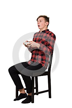 Stunned boy teenager seated on a chair playing video games isolated over white background. Frightened guy stand all ears holding a