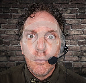 Stunned Businessman Wearing Phone Headset In Office With Brick Wall Background