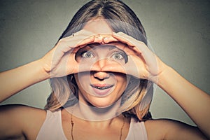 Stunned curious woman, peeking looking through fingers like binoculars