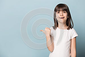 Stunned little girl looks at camera point finger on copyspace
