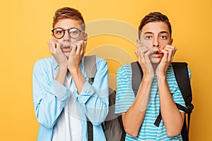 Stunned, shocked, two guys, teenagers are choking with fear, cover their mouths with both hands, on a yellow background