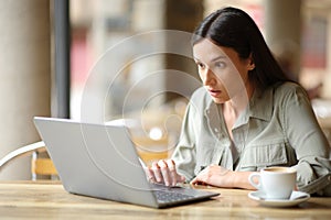 Stunned woman checking news on laptop in a bar photo