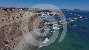 Stunning aerial footage of the vast blue ocean water and waves crashing into the rocks with people walking on the beach