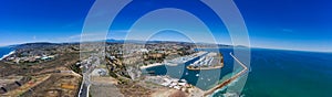 A stunning aerial panoramic shot of the deep blue ocean water and the sandy beach and the boats on the harbor