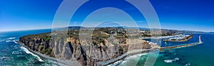 A stunning aerial panoramic shot of the deep blue ocean water and the sandy beach and the boats on the harbor