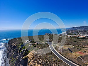 A stunning aerial shot of the coastline with vast blue and green ocean water, lush green hillsides with homes and waves