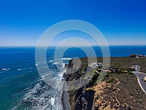 A stunning aerial shot of the coastline with vast blue and green ocean water, lush green hillsides with homes and waves