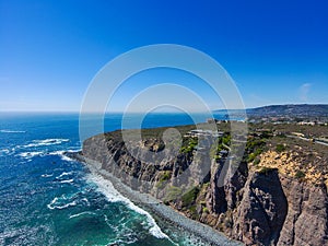 A stunning aerial shot of the coastline with vast blue and green ocean water, lush green hillsides with homes and waves