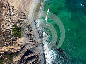 A stunning aerial shot of the gorgeous green ocean water with waves rolling into the beach and crashing into the rocks