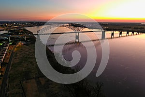 A stunning aerial shot of a long metal bridge over the Mississippi river at sunset with a gorgeous blue, yellow and orange sky