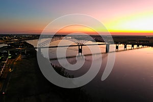 A stunning aerial shot of a long metal bridge over the Mississippi river at sunset with a gorgeous blue, yellow and orange sky