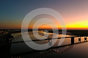 A stunning aerial shot of a long metal bridge over the Mississippi river at sunset with a gorgeous blue, yellow and orange sky