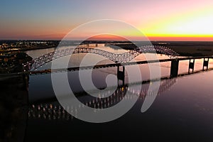 A stunning aerial shot of a long metal bridge over the Mississippi river at sunset with a gorgeous blue, yellow and orange sky