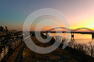 A stunning aerial shot of a long metal bridge over the Mississippi river at sunset with a gorgeous blue, yellow and orange sky