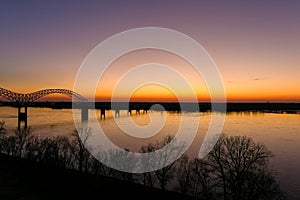 A stunning aerial shot of a long metal bridge over the Mississippi river at sunset with a gorgeous blue, yellow and orange sky