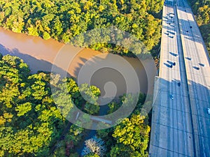 A stunning aerial shot of the lush brown waters of the river and the freeway with cars running across it