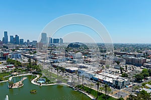 A stunning aerial shot of silky green lake in the park surrounded by lush green palm trees, grass and plants with skyscrapers