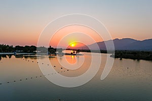 A stunning aerial shot of a sunset over the lake surrounded majestic mountain ranges and lush green trees and grass