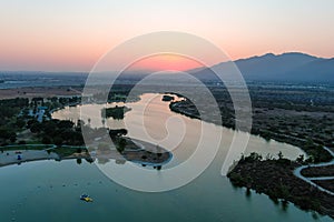 A stunning aerial shot of a sunset over the lake surrounded majestic mountain ranges and lush green trees and grass