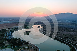 A stunning aerial shot of a sunset over the lake surrounded majestic mountain ranges and lush green trees and grass