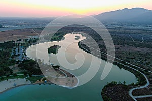 A stunning aerial shot of a sunset over the lake surrounded majestic mountain ranges and lush green trees and grass
