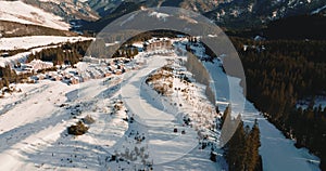 Stunning aerial view of winter holiday vacation resort, chalet houses and snowy mountain trail slope with ski lifts.