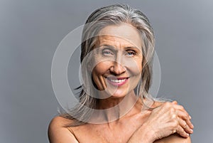 Stunning attractive elderly gray-haired woman look at the camera over grey background