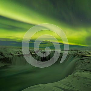 A stunning aurora above the landscape of Godafoss waterfall in winter Iceland. Green northern lights. Starry sky with polar lights