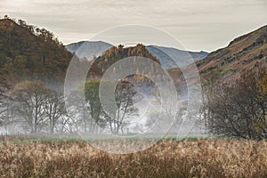 Stunning Autumn landscape sunrise image looking towards Borrowdale Valley from Manesty Park in Lake District with fog rolling