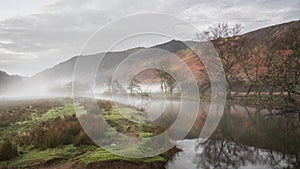 Stunning Autumn landscape sunrise image looking towards Borrowdale Valley from Manesty Park in Lake District with fog rolling