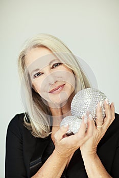 Stunning beautiful and self confident best aged woman with grey hair smiling into camera, holding Christmas decoration baubles