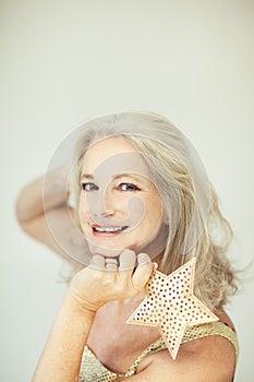 Stunning beautiful and self confident best aged woman with grey hair smiling into camera, holding Christmas decoration star