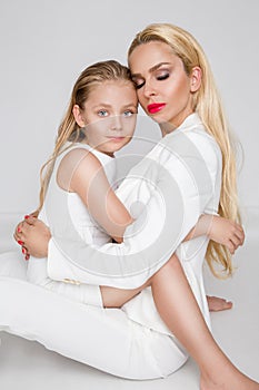 Stunning beauty a young mother with a cute blonde daughter standing on a white background dressed