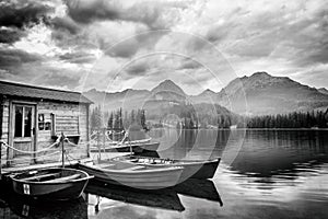 Stunning black and white landscape with cloudy sky, mountains and lake with pleasure boats, Strbske pleso, High Tatras, Slovakia