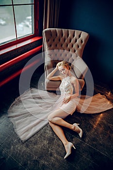 Stunning blonde props her head with her hand and reclines on the black floor