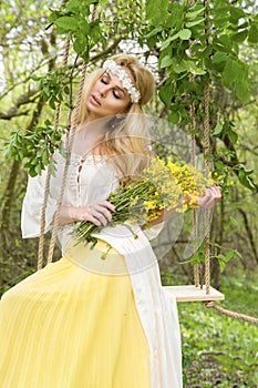 Stunning blonde natural woman swing on a swing on a tree wearing a spring dress