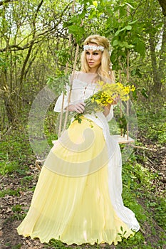 Stunning blonde natural woman swing on a swing on a tree wearing a spring dress