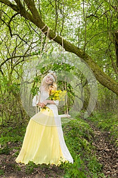 Stunning blonde natural woman swing on a swing on a tree wearing a spring dress