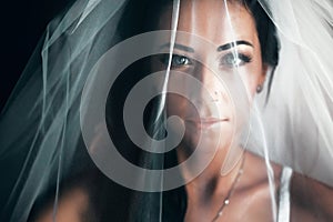 Stunning bride with black hair looks hidden under a veil