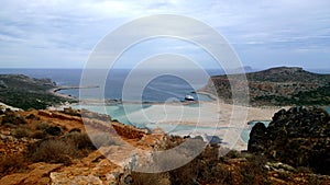 Stunning bright views of the famous Bay of Balos in Crete. Destroyed bright brown wall in foreground, the sea and the ship in the