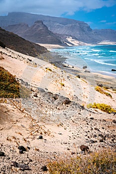 Stunning desolate landscape of sand dunes and desert plants in front of ocean waves on Baia Das Gatas in background