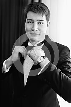 Stunning groom adjusts a black bow tie posing in a hotel room