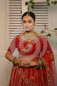 Stunning Indian bride adorned in a traditional red bridal lehenga gracefully wears heavy gold jewelry