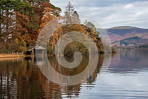 Stunning landscape image of boathouse on Derwentwater during vibrant Autumn sunrise with woodland surrounding the lake