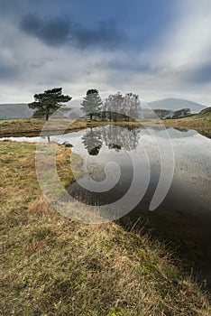 Stunning landscape image of dramatic storm clouds over Kelly Hall Tarn in Lake District during late Autumn Fall afternoon