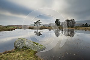 Stunning landscape image of dramatic storm clouds over Kelly Hall Tarn in Lake District during late Autumn Fall afternoon